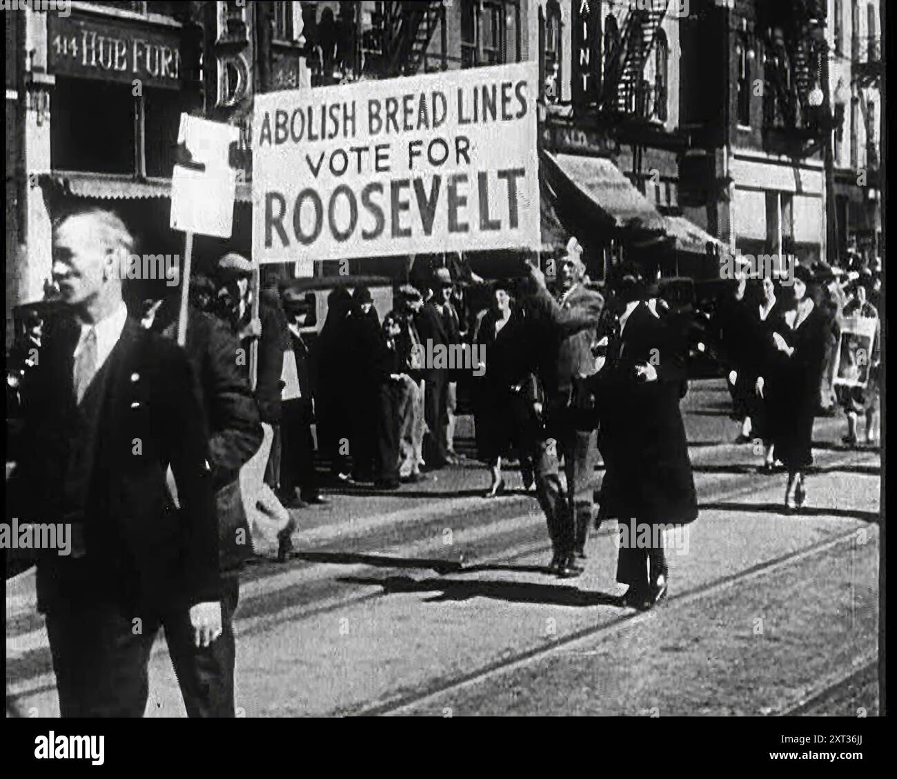 Anhänger beider Präsidentschaftskandidaten marschieren auf der Straße. Auf Dem Schild Steht: "Abschaffung Der Brotlinien - Abstimmung Für Roosevelt", 1932. USA: Franklin D Roosevelt wird bei den Präsidentschaftswahlen als demokratischer Kandidat gewählt. Aber obwohl die Partei überzeugt sein konnte, mussten sie die Leute trotzdem überzeugen. Die Leute, denen man es sagen muss und die man anbeten und flehen muss... denn es sind die Leute, die einen dort hinbringen können, oder dich draußen in der Kälte lassen... also denk gut und entscheide dich, denn die Zukunft einer Nation hängt davon ab. Aus „Time to Remember – Around the Corner“, 1932 (Rolle 3); Tagebuch der Ereignisse in 19 Stockfoto