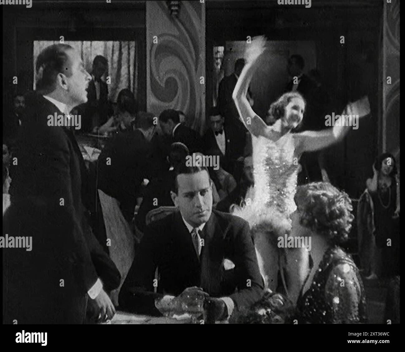Szene aus einem Film aus den 1920er Jahren. Zwei Schauspieler, die ein Paar in einer Nachtclub-Szene darstellen, während eine Band einen Black Bottom oder einen Charleston hinter ihnen spielt, 1920er Jahre „In der [stummen] Filmwelt war das Leben eine ständige Cocktailparty – endlos, aber scheinbar essentiell für die Handlung“. Aus „Time to Remember – Come the Dawn“, 1925 (Reel 2); werfen Sie einen Blick auf die britische Filmindustrie der 1920er Jahre – Clips aus großen Stummfilmen und Wochenschauen. Stockfoto