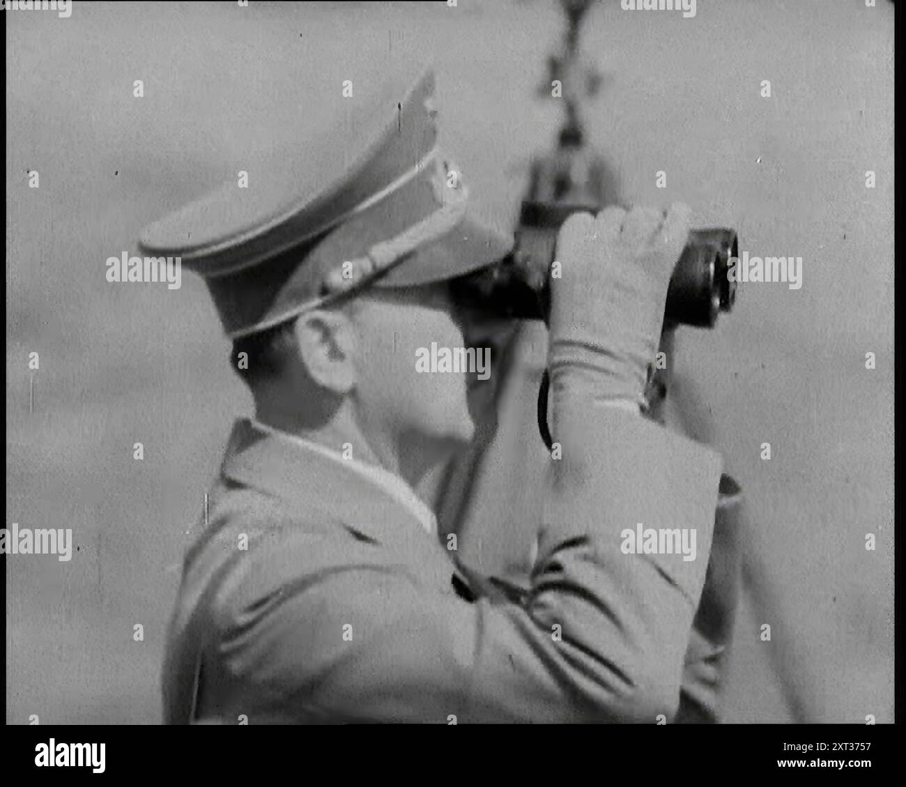 Adolf Hitler, der deutsche Anführer, der durch Ferngläser schaut, bei Armeebeschritten, 1937. "Das neue Nazi-Deutschland schien sehr schnell neu zu bewaffnen. Neue Spielzeuge für junge Deutsche, während der, der sie gegeben hatte, ihre Spiele mit Zufriedenheit beobachtete. Ja, für den Führer haben sich seine Pläne gut entwickelt. Die erste seiner neuen Autobahnen war eröffnet worden, und wer sollte dann erkennen, dass ihr wahrer Zweck für den schnellen Transport von Truppen war. Aus "Time to Remember - Sense of Values", 1937 (Reel 3); Dokumentarfilm über die Ereignisse von 1937, Krieg im Fernen Osten, Aufbau bis Krieg in Europa. Stockfoto