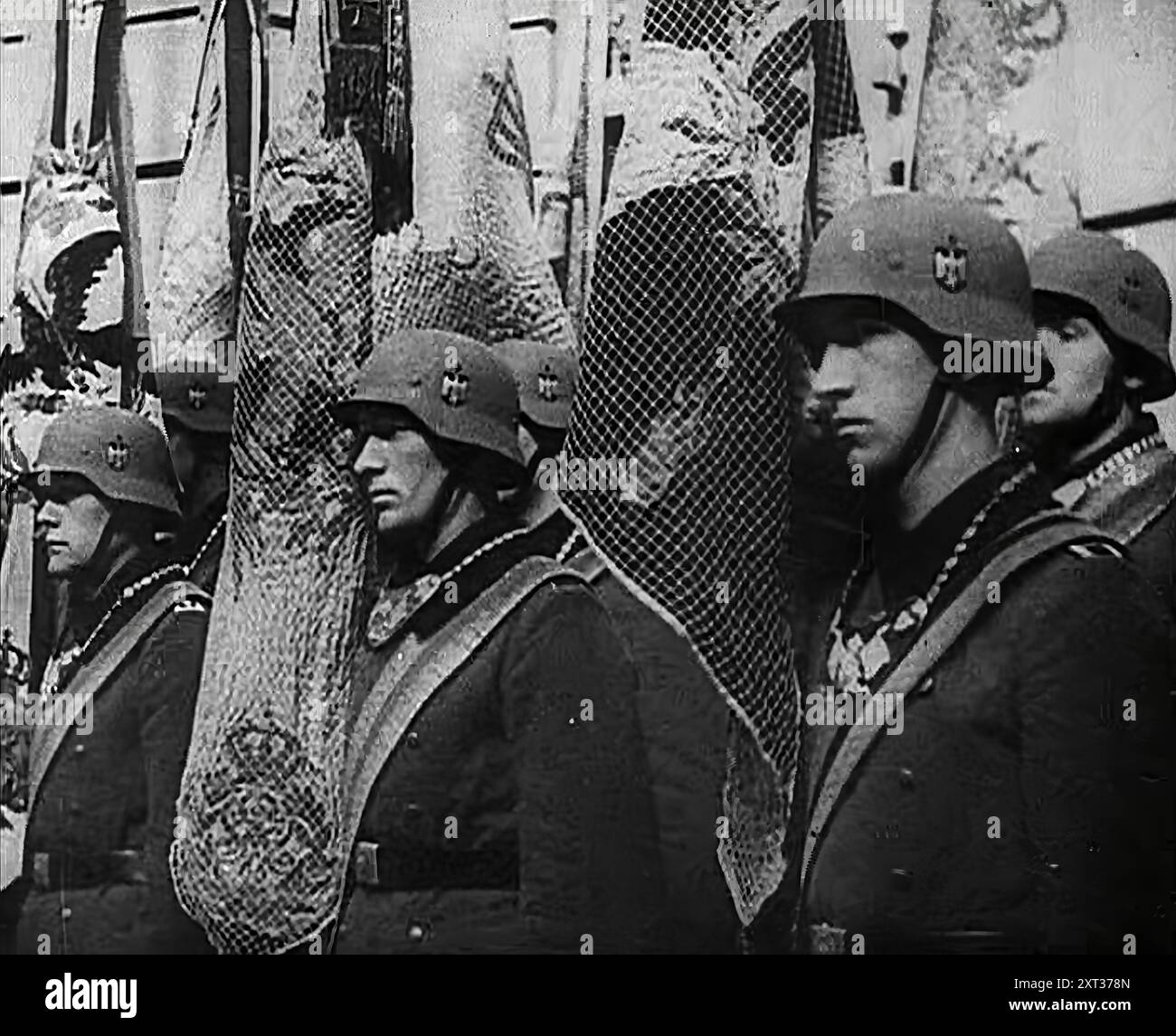Deutsche Soldaten Stehen Mit Fahnen, 1941. Zweiter Weltkrieg. "...der Feind auf der anderen Seite des Kanals [d. h. Hitler] war gezwungen, seinen fruchtbaren Geist anderen und noch ehrgeizigeren Konzepten zuzuwenden... die Nazi-Hierarchie wandte ihre Machenschaften - ohne ein wenig Angst - auf die bedeutsame Operation Barbarossa." Aus „Time to Remember – Operation Barbarossa“, 1941 (Rolle 1); Dokumentarfilm über Ereignisse von 1941, an der Ostfront und in Pearl Harbour. Stockfoto