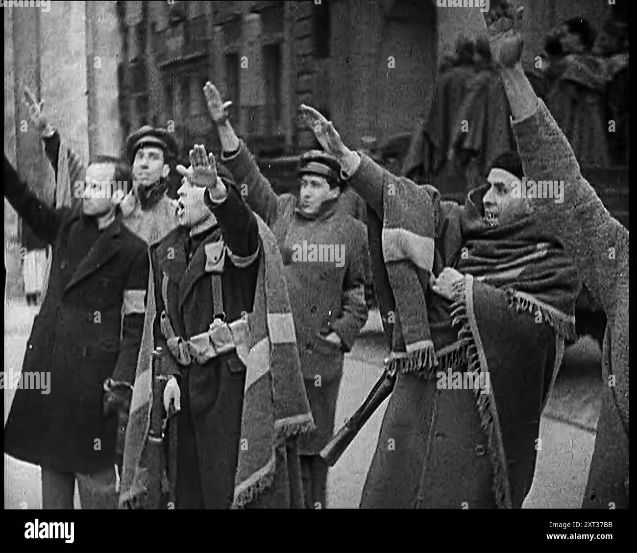 Bewaffnete Männer und Zivilisten, die in einer Straße in Madrid faschistische Grußworte machen, alle in dicken Mänteln und zwei mit Decken um die Schultern gekleidet, 1939. Aus „Time to Remember – The Reluctant Warriors“, 1939 (Reel 1); Dokumentarfilm über Ereignisse von 1939 – Vorbereitungen für den Krieg und dann Feindseligkeiten brechen aus. Stockfoto