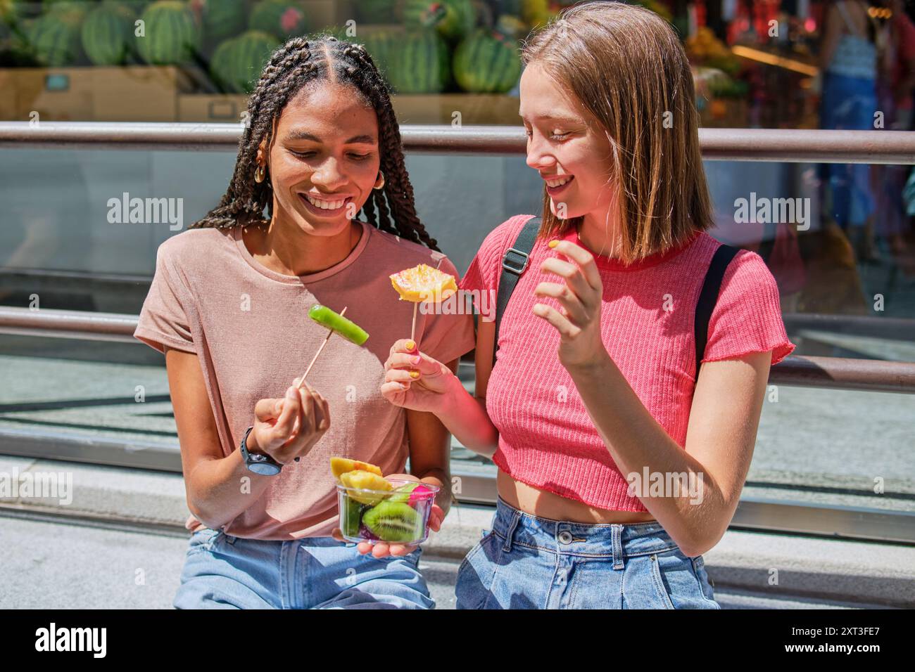 Zwei Freunde, die an einem sonnigen Tag frisches Obst essen. Sie lächeln und spiegeln eine warme, freundliche Atmosphäre wider. Stockfoto