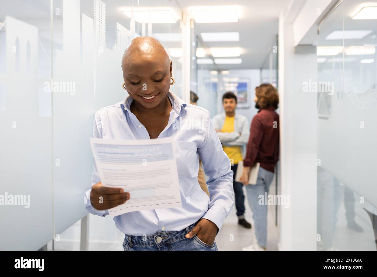Eine junge Frau liest in einem belebten Akademiekorridor Vorträge und betont dabei die Teamarbeit in einer Englisch-Lernumgebung, in der Kollegen an Diskussionen teilnehmen Stockfoto