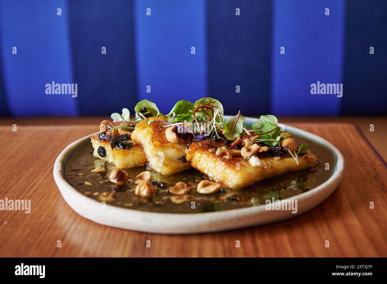 Dieses herzhafte Gourmetgericht besteht aus goldbraunem halloumi-Käse, garniert mit frischem Gemüse und knusprigen Haselnüssen, serviert auf einer Keramikplatte Stockfoto