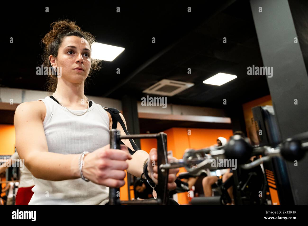 Eine entschlossene junge Frau nimmt an einem Krafttraining Teil, wobei sie Gewichte und schwere Geräte in einem modernen, gut beleuchteten Fitnessstudio benutzt Stockfoto