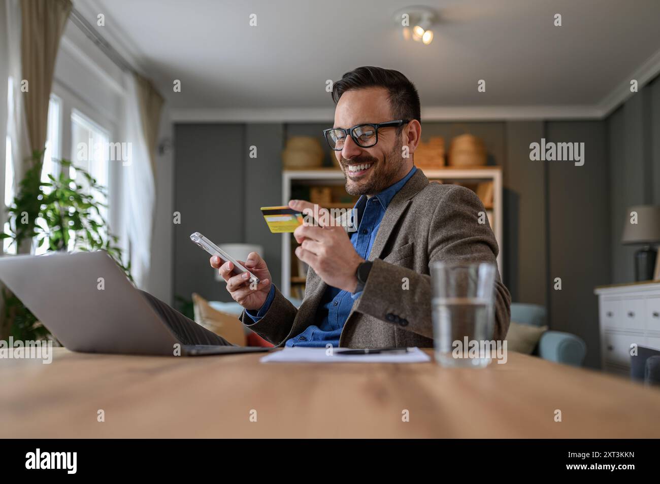 Flacher Blick auf männliche Profis, die mit Kreditkarte über Smartphone bezahlen, während sie am Schreibtisch sitzen Stockfoto