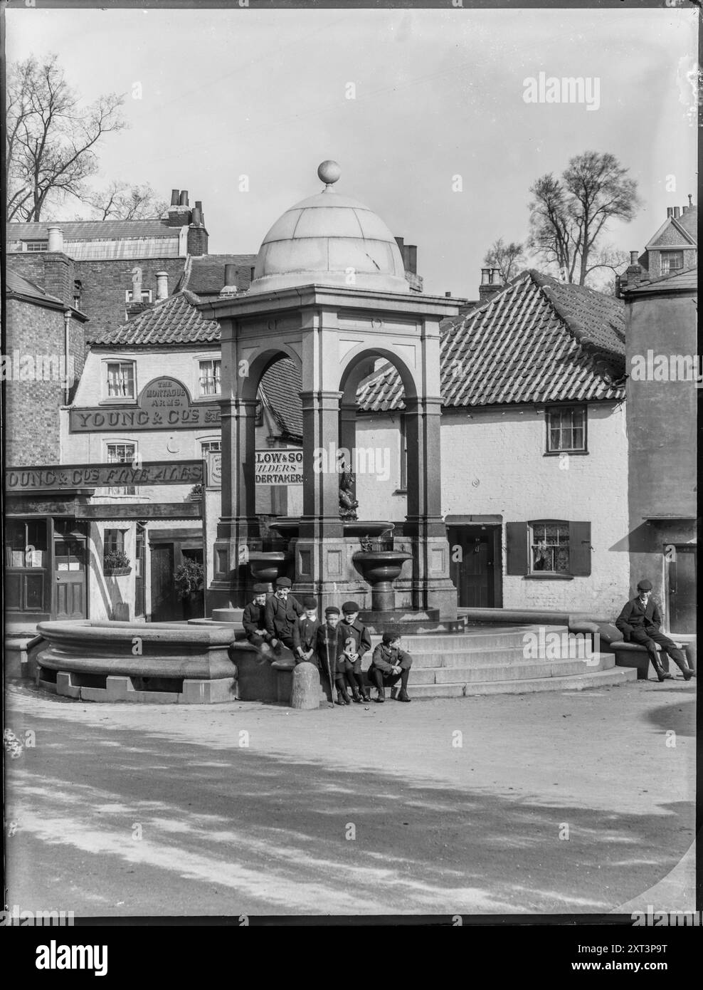 Trinkbrunnen, Roehampton Lane, Roehampton, Wandsworth, Greater London Authority, 1904. eine Gruppe von Jungen versammelte sich auf der Treppe am Fuße des Trinkbrunnens an der Kreuzung von Medfield Street und Roehampton Lane, wobei die Montague-Arme im Hintergrund sichtbar waren. Der Brunnen wurde 1882 nach den Plänen von Sir Frederick Lance für Mrs. Lyne Stephens aus Grove House erbaut. Ein Detail dieser Fotografie erscheint in William Fields Photographs of Putney, zusammengestellt von Dorian Gerhold und Michael Bull für die Wandsworth Historical Society. Stockfoto