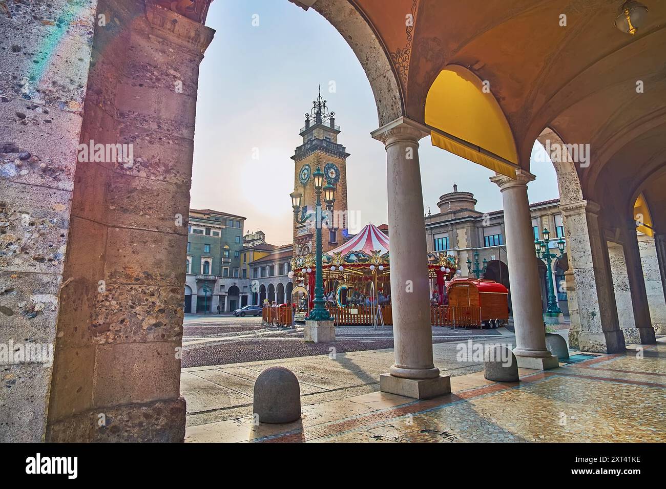 Der hohe Stein-Gedenkturm und das Vintage-Karussell vom Säulengang des Piacentiniano Centre, Piazza Vittorio Veneto, Citta Bassa, Bergamo, Italien Stockfoto