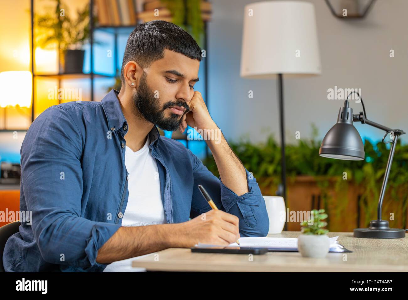 Indischer bärtiger Mann, der freiberuflich mit Dokumenten aus dem Home Office arbeitet, Informationen analysiert, Geschäftsberichte liest, Finanzberichte erstellt. Junger hispanischer Buchhalter, der Diagrammdokumente analysiert. Stockfoto