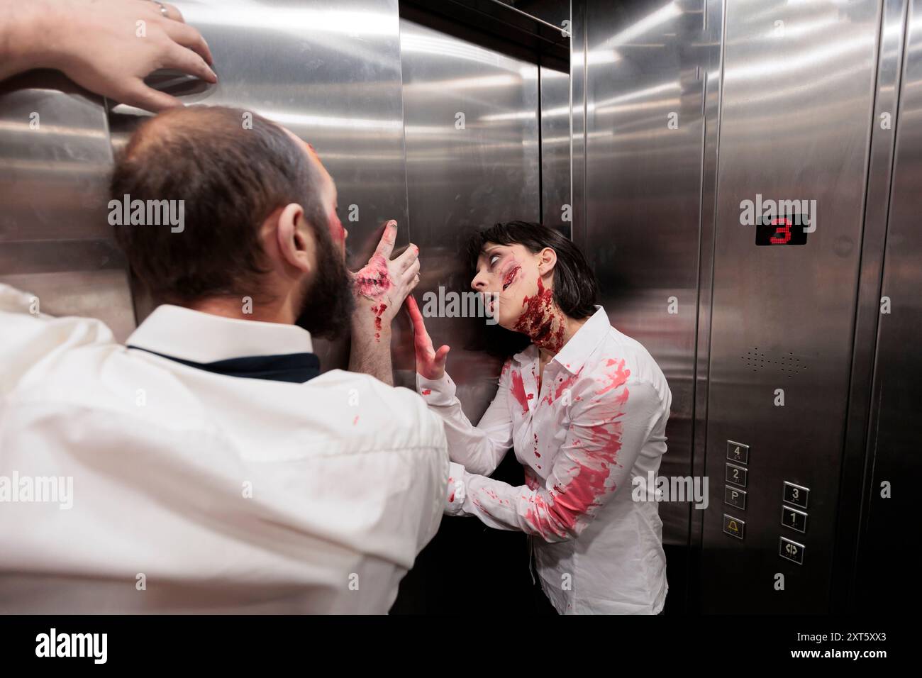 Schauspieler spielen in der Horrorfilmszene gefährliche Zombies, die so tun, als wären sie im Fahrstuhl stecken geblieben. Mann und Frau, bedeckt mit gefälschtem Blut, mit untoten Kreaturen, Rolle in Thriller-Film in Rolltreppe Stockfoto