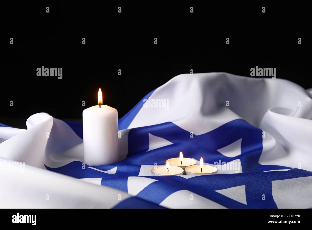 Brennende Kerzen und große Flagge Israels auf dunklem Hintergrund. Holocaust-Gedenktag Stockfoto