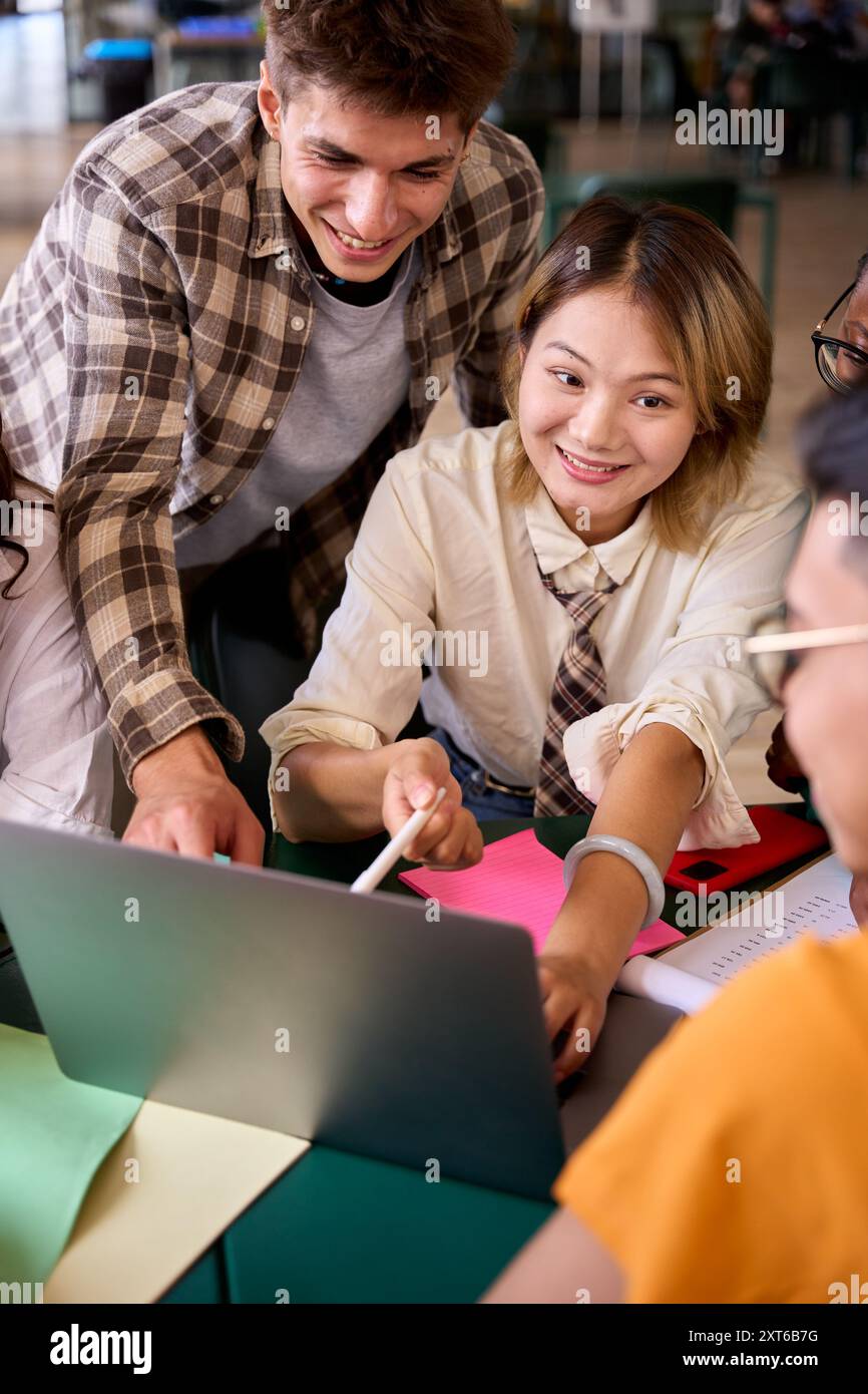 Eine Gruppe von verschiedenen, lächelnden jungen Studenten, die sich mit einem Laptop im Klassenzimmer der Universität versammeln. Stockfoto