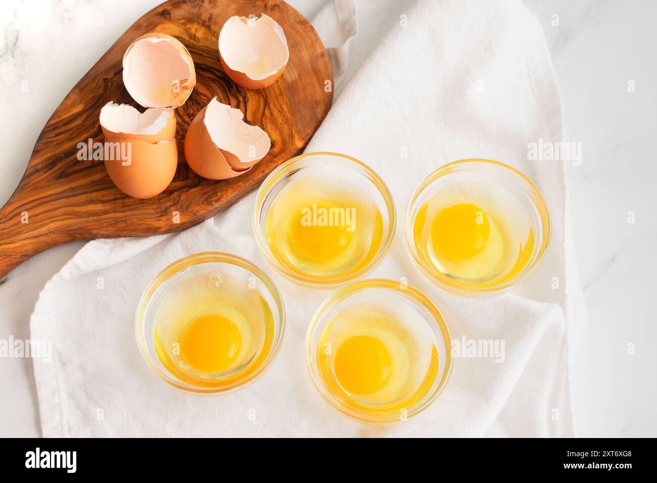Eier in kleine Glasschalen zerrissen: Rohe Eier in kleine Glasschüsseln auf einer Marmorküche Stockfoto