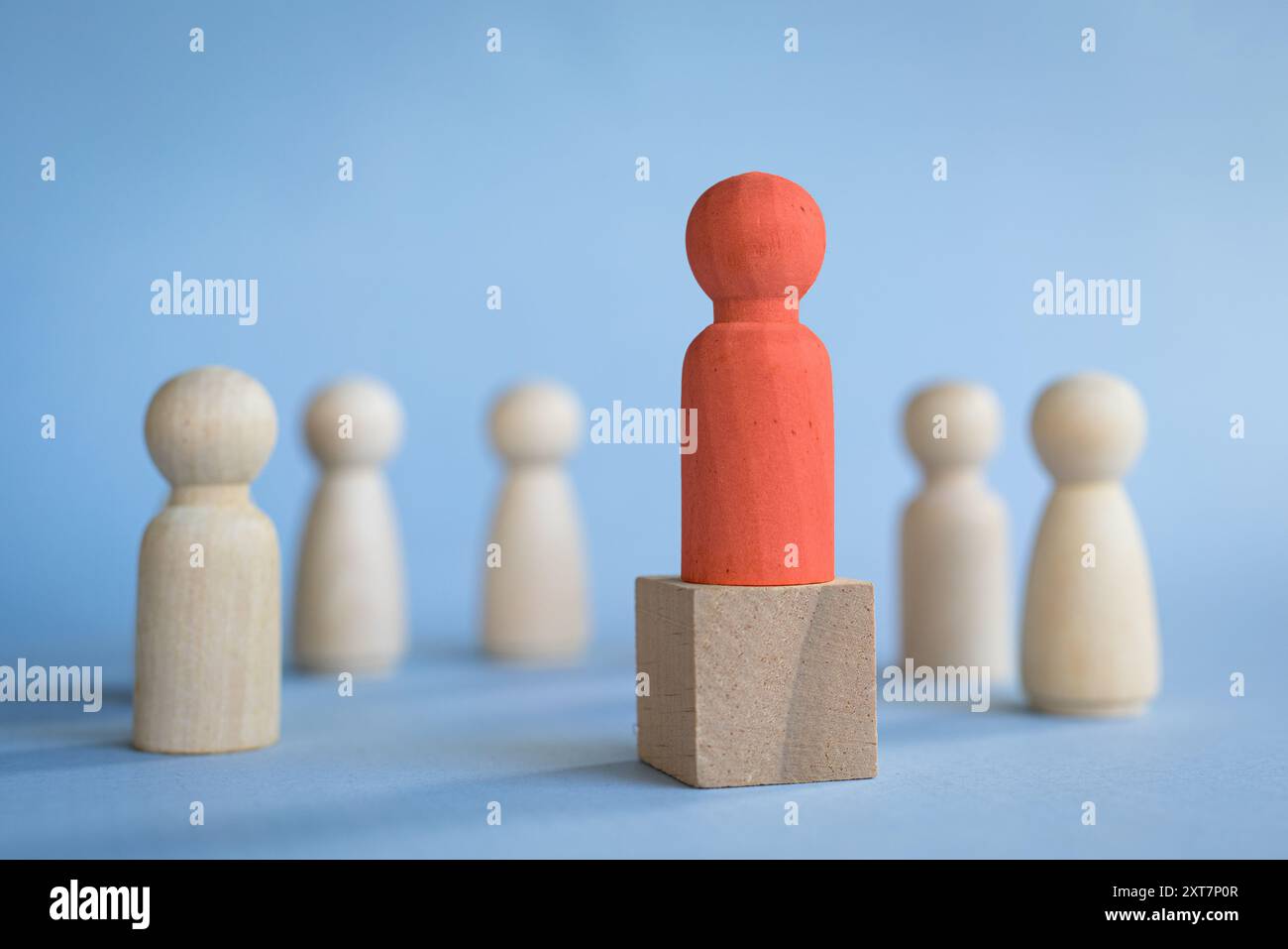 Roter Spielzeugblock steht auf dem Podium gegenüber anderen Spielzeugblöcken, die auf einem Halbkreis stehen. Veranschaulichen Sie das Führungskonzept. Stockfoto