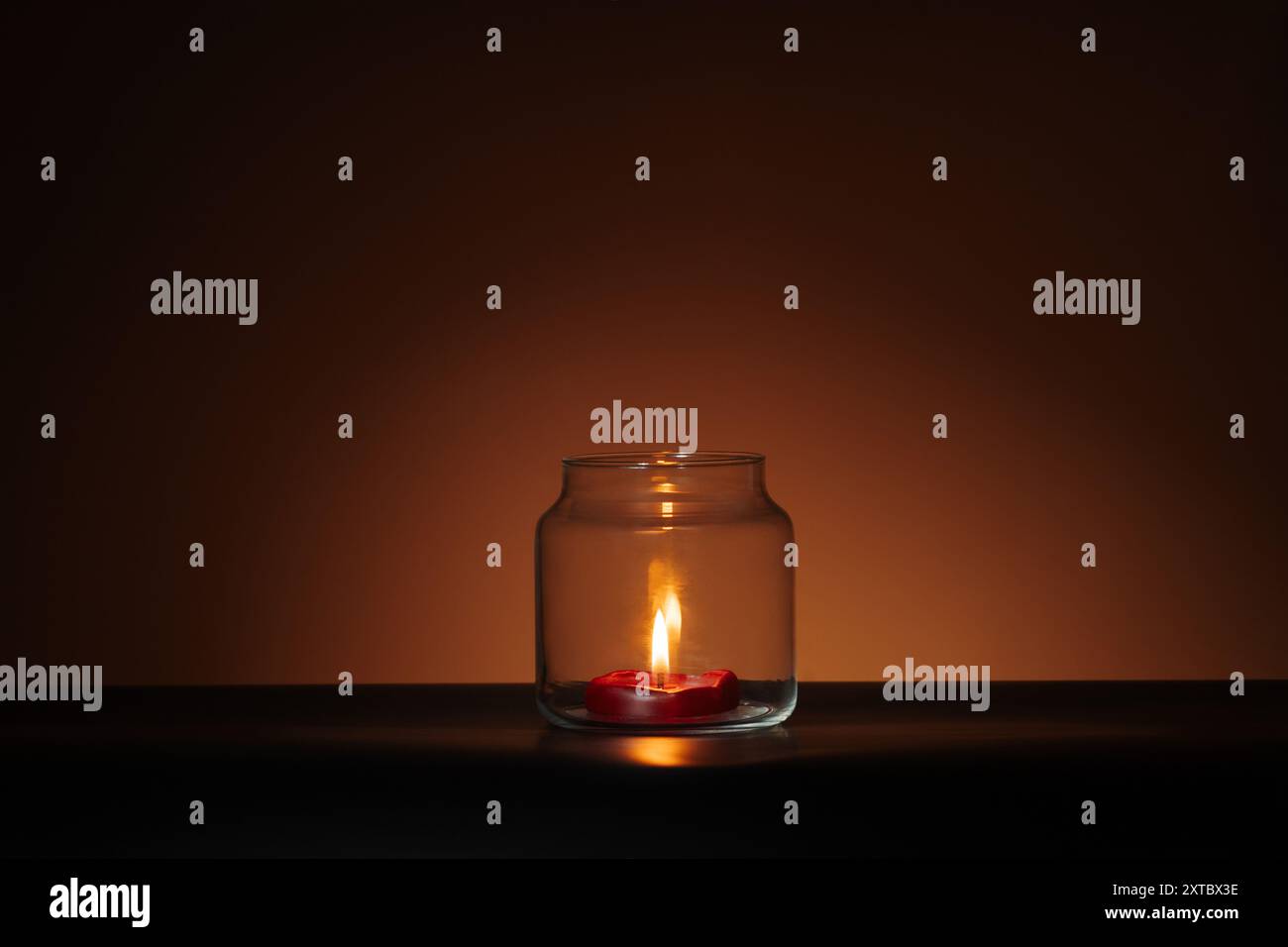Rote Kerze im Glas auf orangefarbenem Halloween-Hintergrund. Gruseliges minimalistisches Banner Stockfoto
