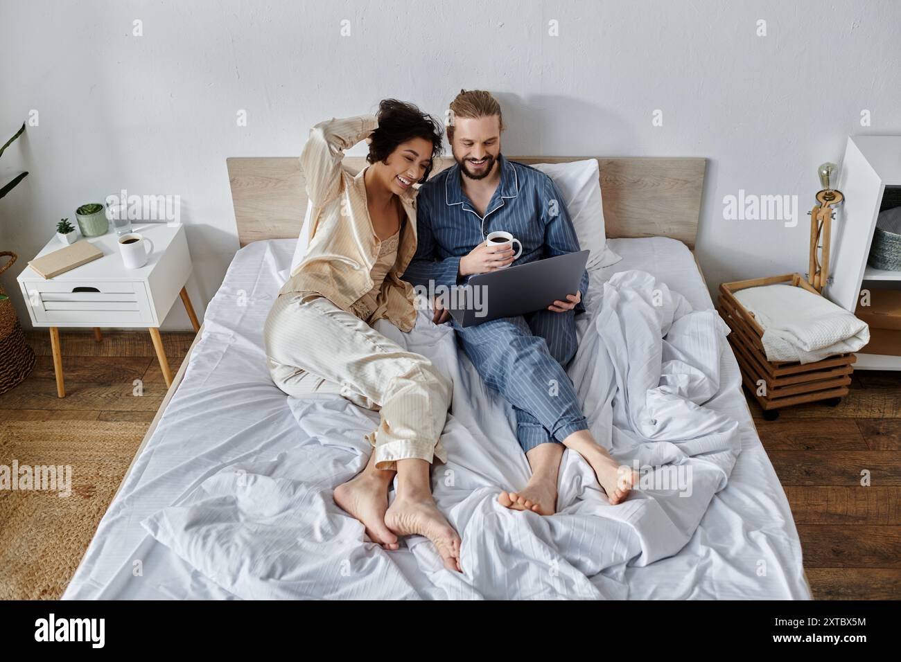 Ein liebevolles Paar kuschelt sich im Bett, genießt Kaffee und benutzt einen Laptop. Stockfoto
