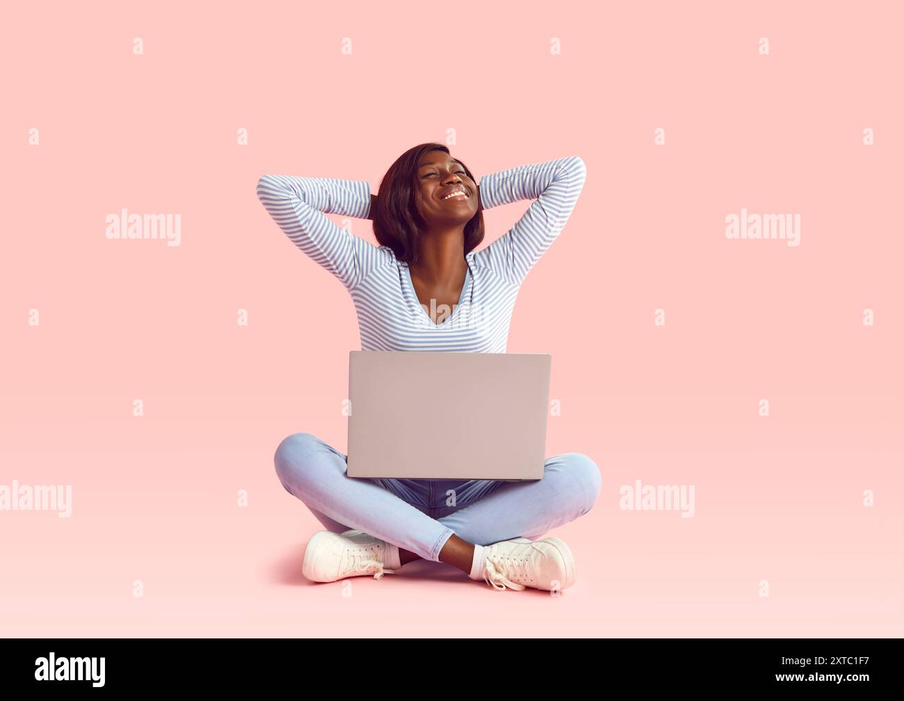 Schwarze Frau sitzt mit Laptop und lächelndem rosa Hintergrund. Der Ausdruck einer schwarzen Frau strahlt Zufriedenheit und Befähigung der modernen schwarzen Frau aus Stockfoto