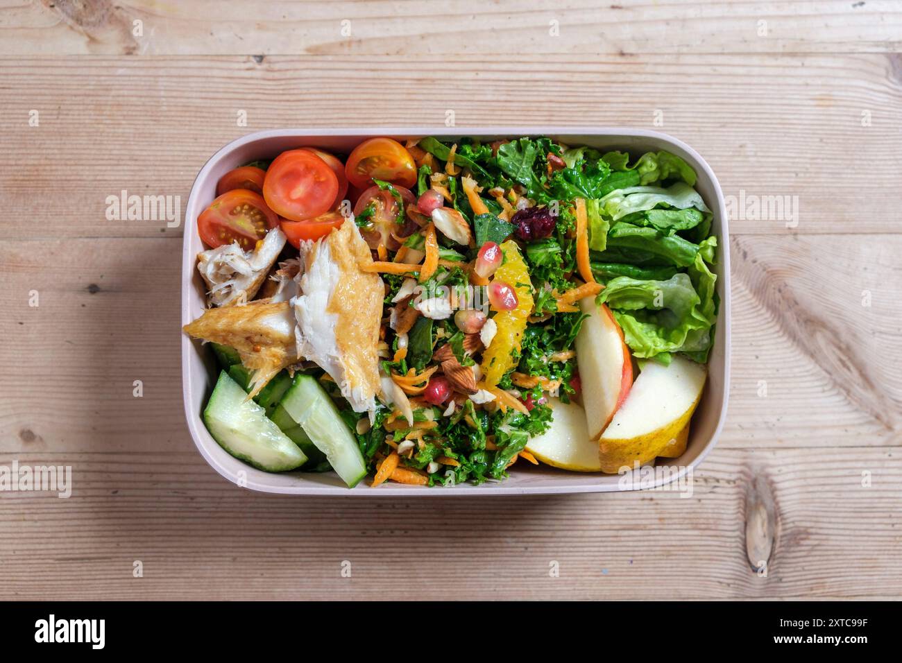 Eine Lunchbox aus Plastik mit hausgemachtem frischem Salat, Tomaten, geschnittenem Apfel und geräuchertem Makrelenfilet. Stockfoto