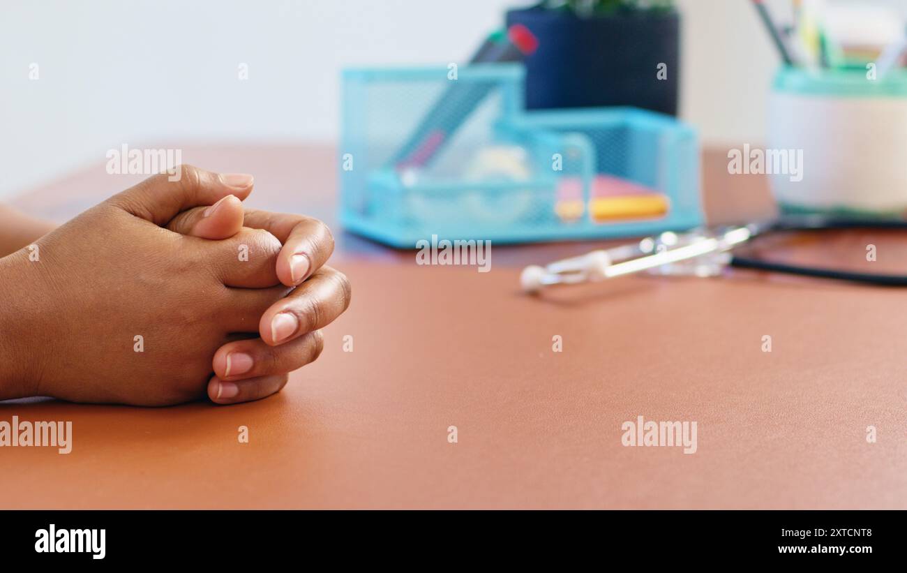 Nahaufnahme der auf einem Schreibtisch gefalteten Hände eines Patienten in einer Arztpraxis Stockfoto