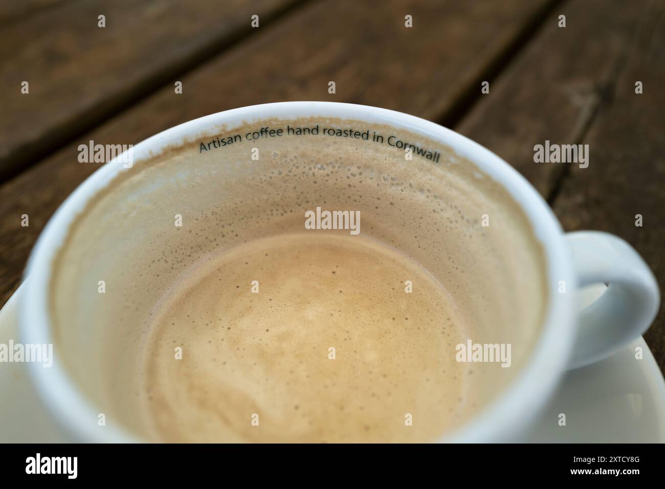 Der Slogan „Artisan Coffee Hand geröstet in Cornwall“ ist auf der Innenseite einer Kaffeetasse mit den Überresten eines flachen weißen Kaffees aufgedruckt. Stockfoto