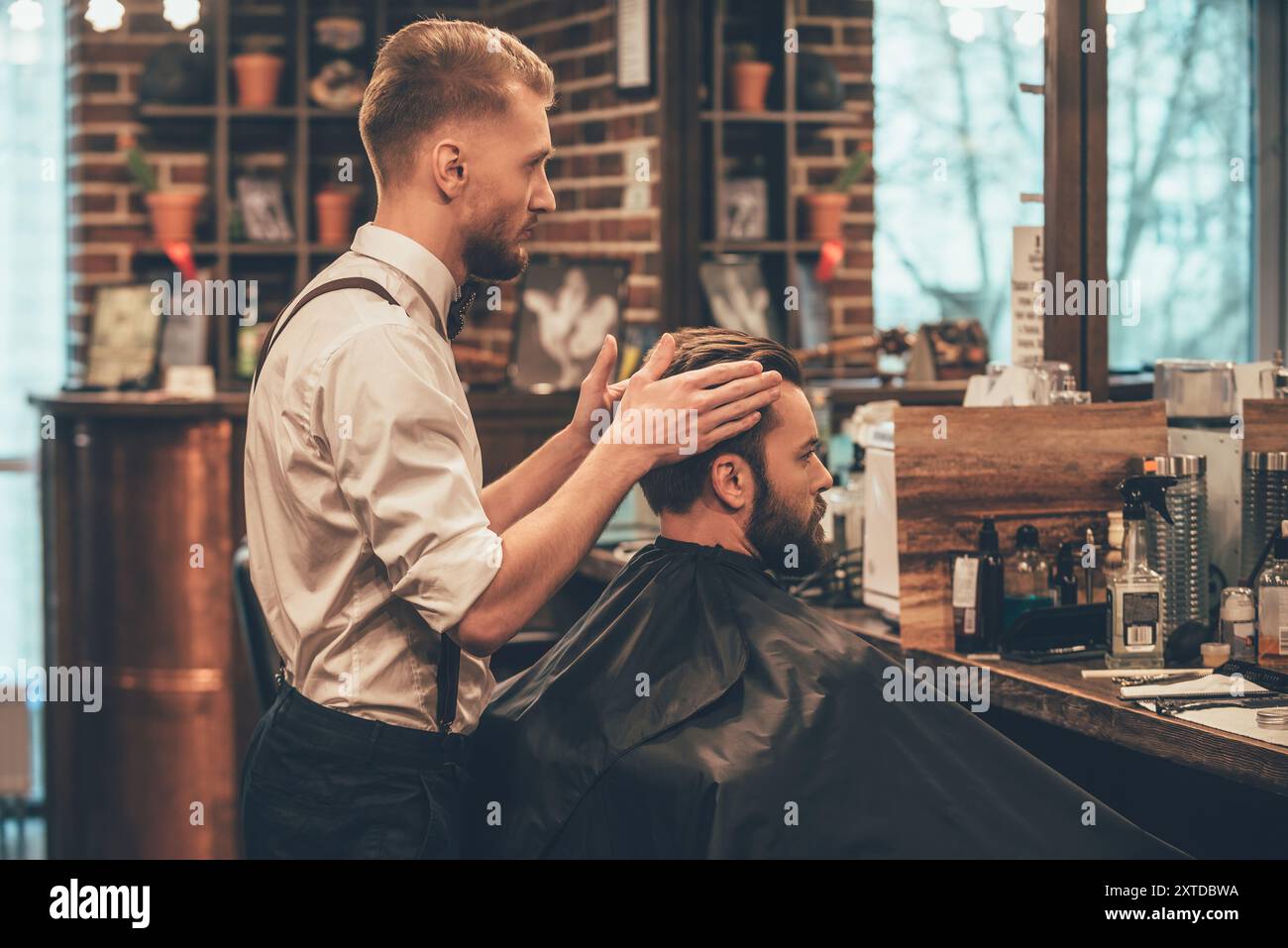 Den letzten Schliff. Seitenansicht der Friseur Kontrolle Symmetrie der Haarschnitt seines Klienten an Barbershop Stockfoto