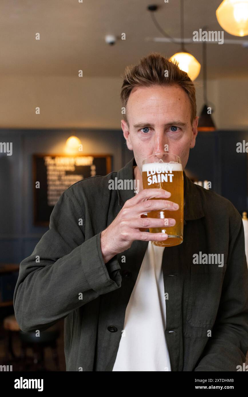 Luke Boase, Gründer und CEO der alkoholfreien Biermarke Lucky Saint, fotografierte mit seinem alkoholfreien Bier in einem Londoner Pub in England, Großbritannien Stockfoto