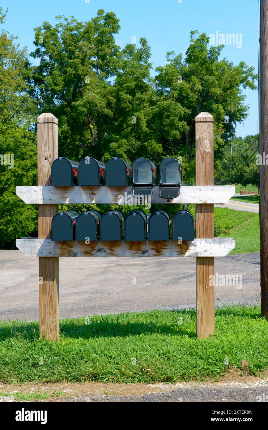 Vertikale Aufnahme von elf unmarkierten schwarzen Briefkästen auf zwei Regalen eines Holzständers. Fünf auf den einen und sechs auf den anderen. Stockfoto