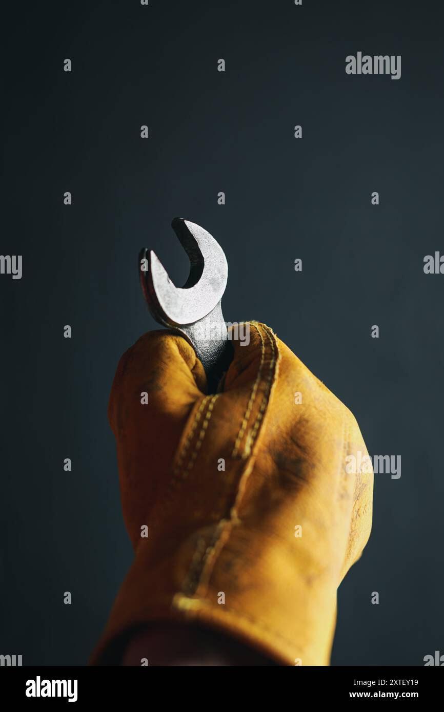 Alter abgenutzter Arbeitshandschuh mit einem Sichelschlüssel. Gewerbearbeit, Arbeiter oder Labor Day-Konzept. Stockfoto