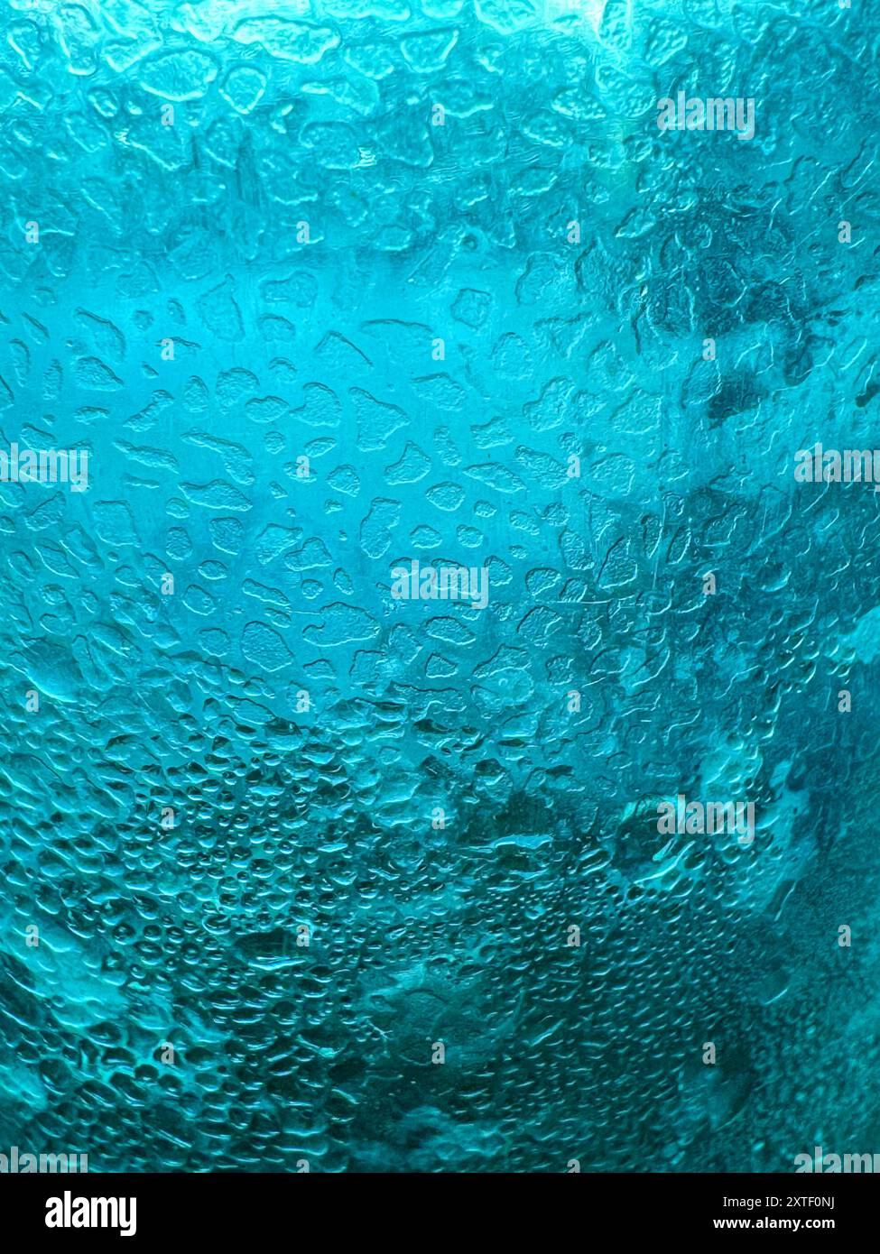 Die Makroaufnahme zeigt Eiskristalle, die sich auf einem farbenfrohen Getränkeglas bilden, wodurch ein lebendiges strukturiertes Muster entsteht, das als grafisches Element verwendet werden kann. Stockfoto