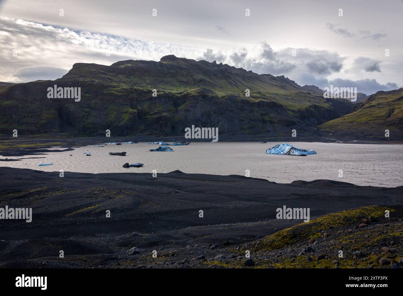 Solheimajokull, Teil des Myrdalsjokull-Gletschers, Gletscherlagune mit schwimmenden blauen Eisbergen und roher Berglandschaft, Island. Stockfoto