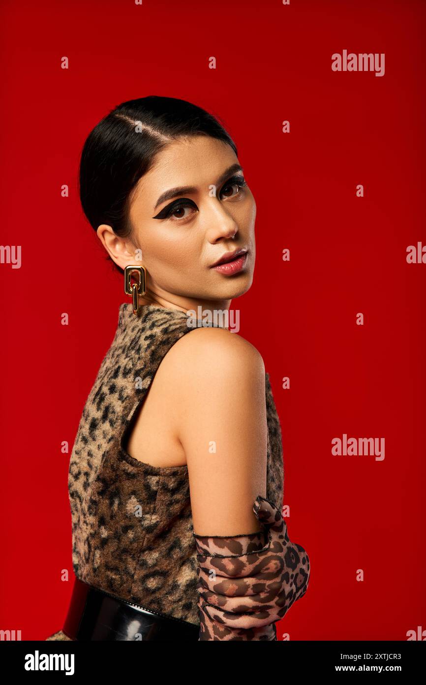 Eine junge Frau posiert in einem Kleid mit Leopardenmuster und Handschuhen vor rotem Hintergrund. Stockfoto