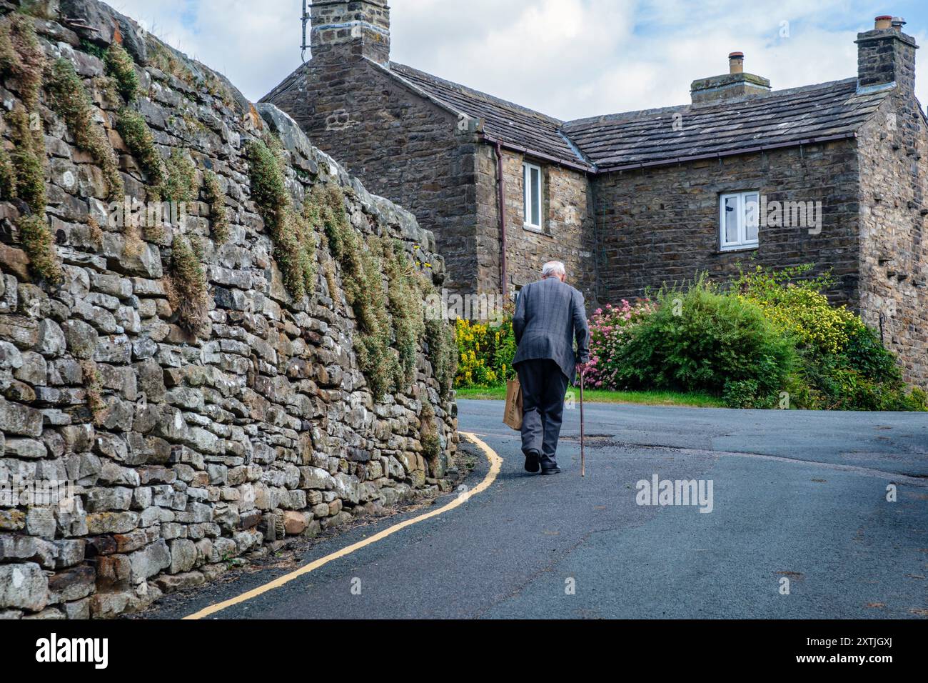 Ein alter Mann, der durch das Yorkshire Dales Dorf Muker, Swaledale, North Yorkshire spaziert Stockfoto