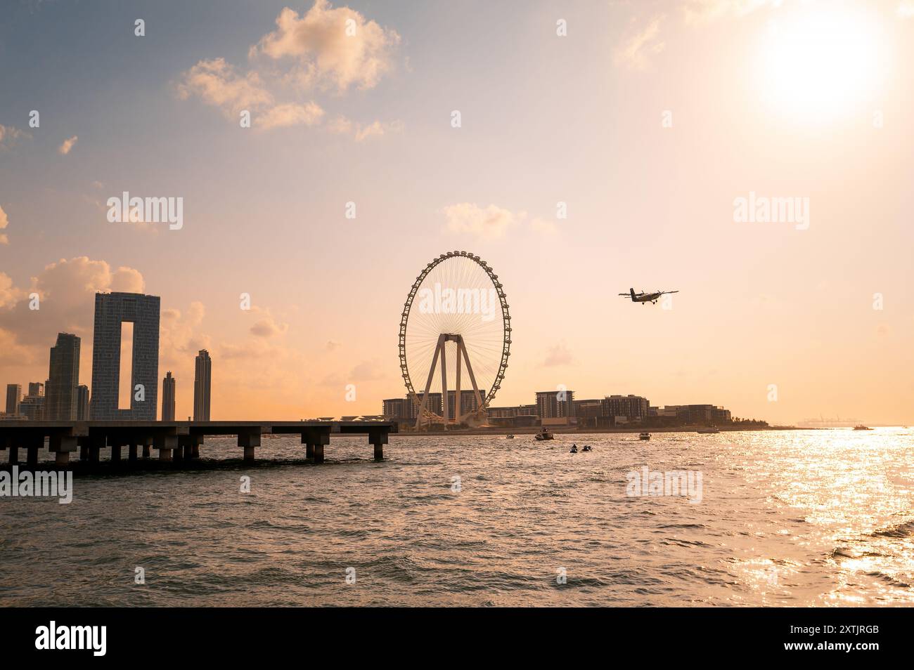 Dubai Marina bei Sonnenuntergang auf einer fesselnden Yachtfahrt. Erleben Sie den bezaubernden Anblick eines Karussells entlang der Küste, begleitet von der anmutigen Silhou Stockfoto