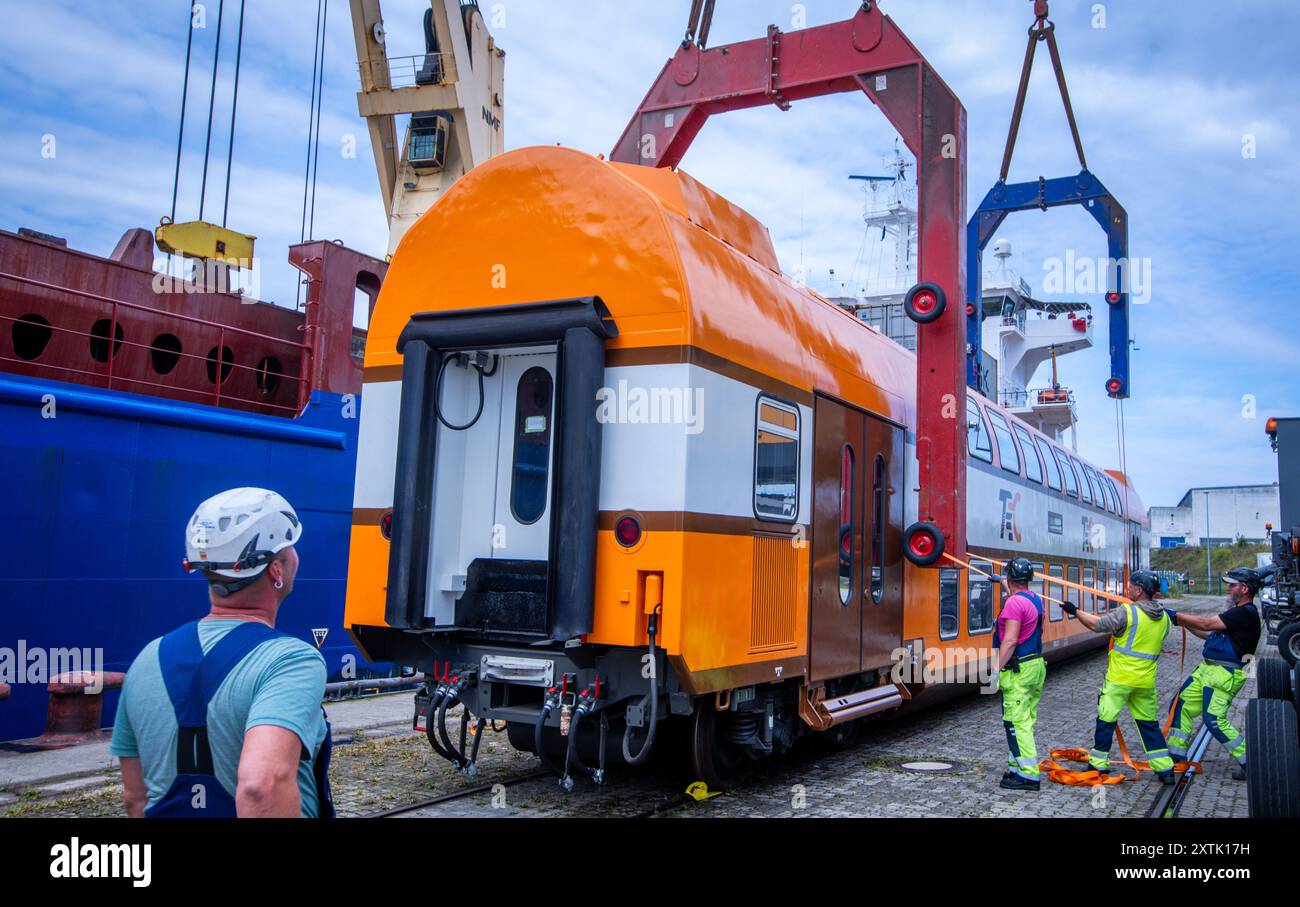 Mukran, Deutschland. August 2024. Die Hafenarbeiter bereiten die modernisierten Doppelstockwagen für die Verladung auf den Schwerlastfrachter „BBC Amber“ vor. Insgesamt werden 30 Doppelstockwagen aus ausgemustertem Bestand der Deutschen Bahn AG und zwei Lokomotiven von der Insel Rügen nach Tansania transportiert. Die Baltic Port Services GmbH (BPS) hatte die Schienenfahrzeuge für den Betrieb in Tansania umgerüstet. Der Kunde, die Tanzania Railways Corporation (TRC), plant, die Doppelstockwagen im Jahr 2024 auf seinem Schienennetz einzusetzen. Quelle: Jens Büttner/dpa/Alamy Live News Stockfoto
