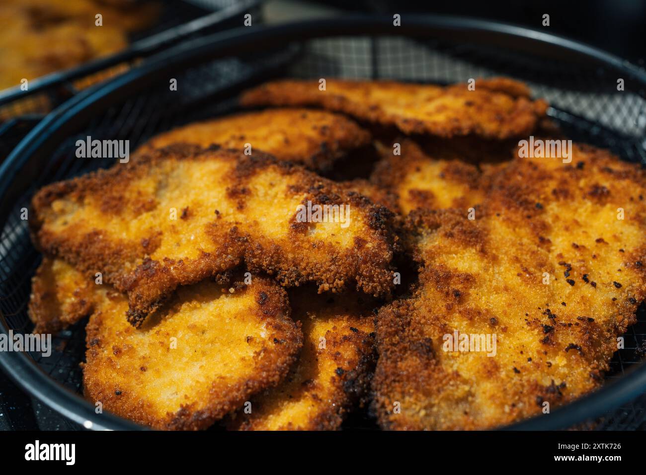 Korb gefüllt mit goldbraunen, knusprigen, hausgemachten, panierten Hühnchenkoteletts, frisch zubereitet und servierfertig. Die Nahaufnahme hebt die knusprige Textur und das köstliche Aussehen des Schnitzels hervor. Stockfoto