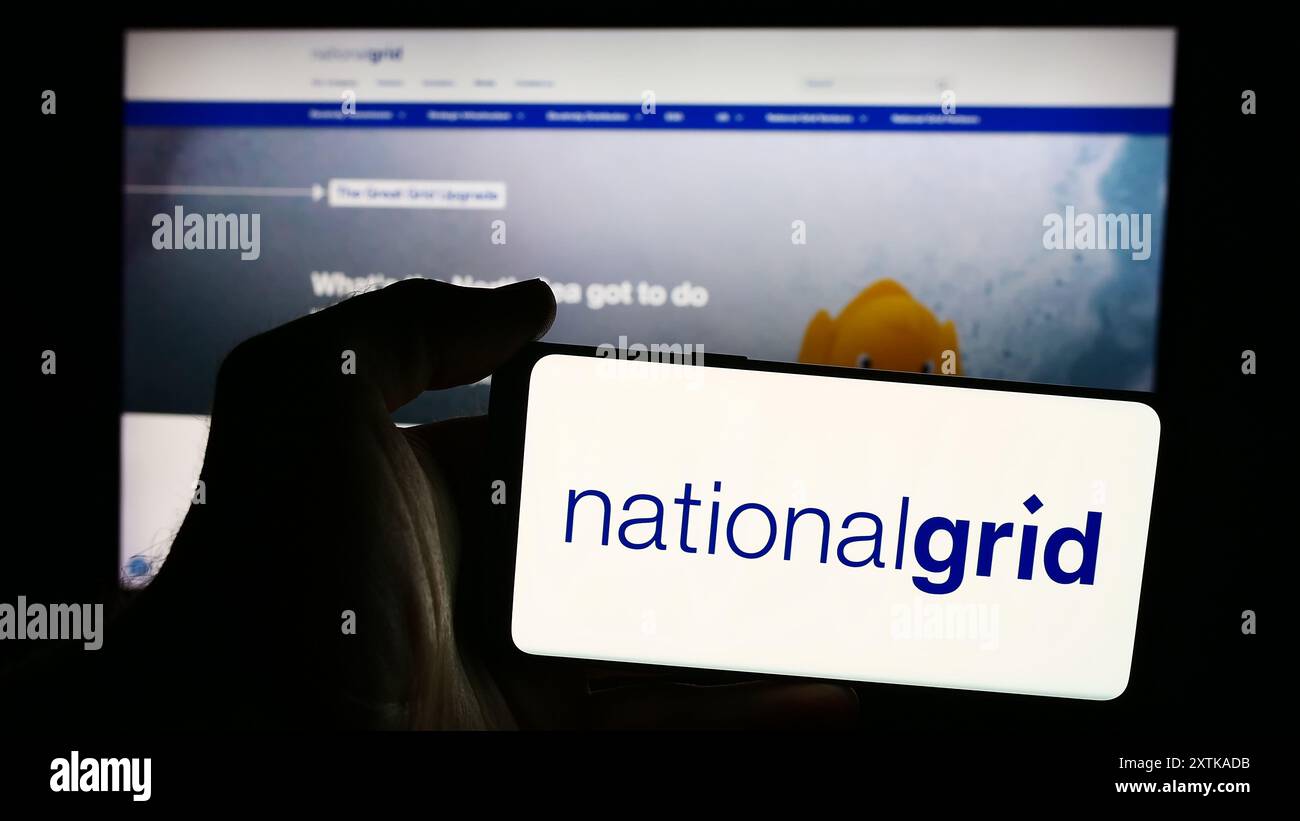 Person, die ein Mobiltelefon mit dem Logo des britischen Energieversorgers National Grid plc vor der Business-Webseite hält. Schwerpunkt auf dem Display des Telefons. Stockfoto