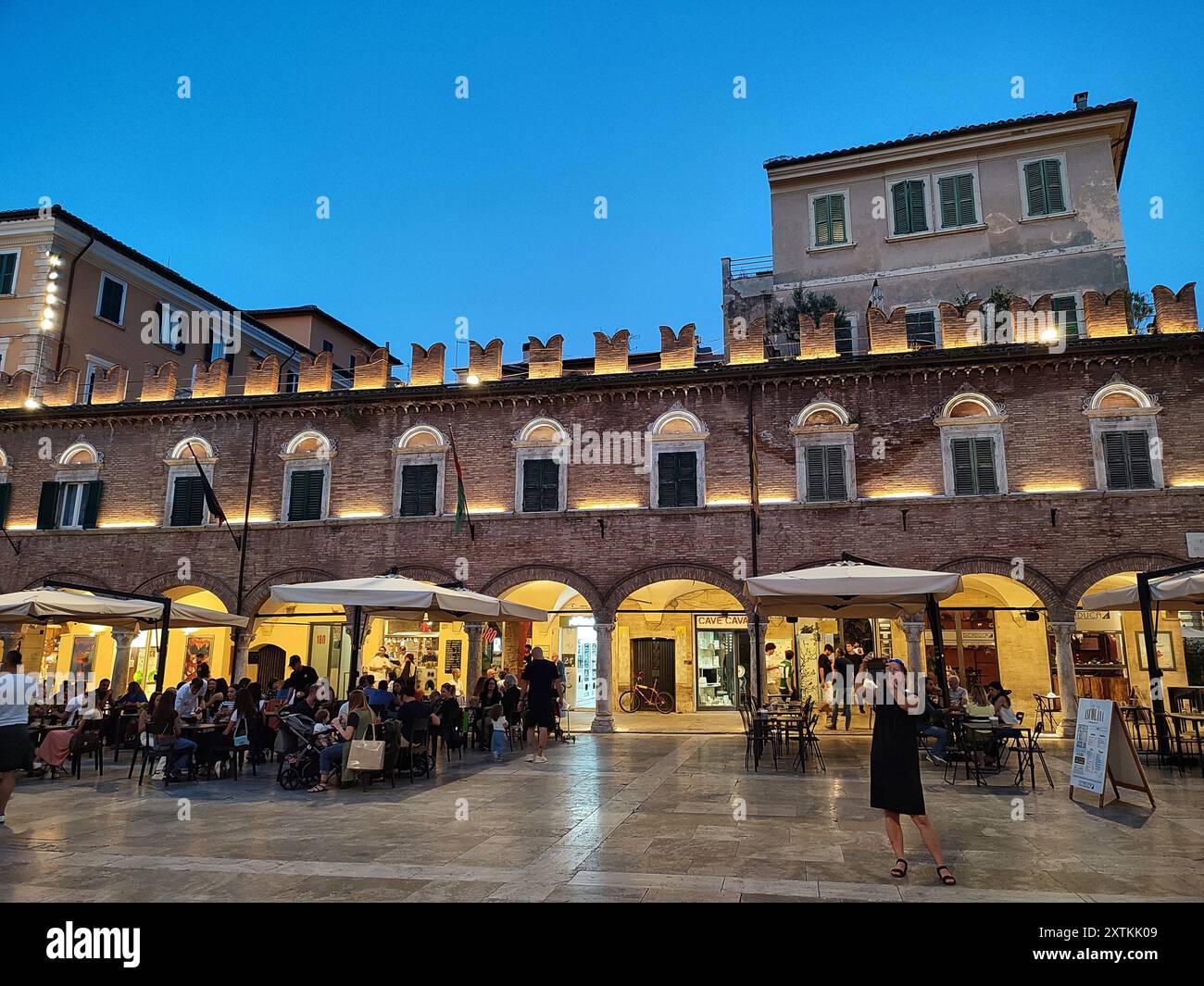 Foto di una piazza illuminata con palazzi storici e turisti seduti al bar Stockfoto