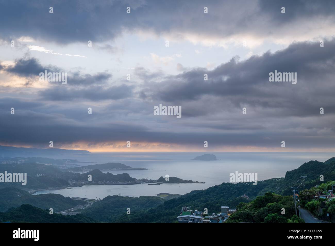 Von der Spitze des Berges aus entfaltet sich eine nebelbehüllte Landschaft, die ein malerisches Küstendorf inmitten sanfter Hügel zeigt. Jiufen, Taiwan. Stockfoto