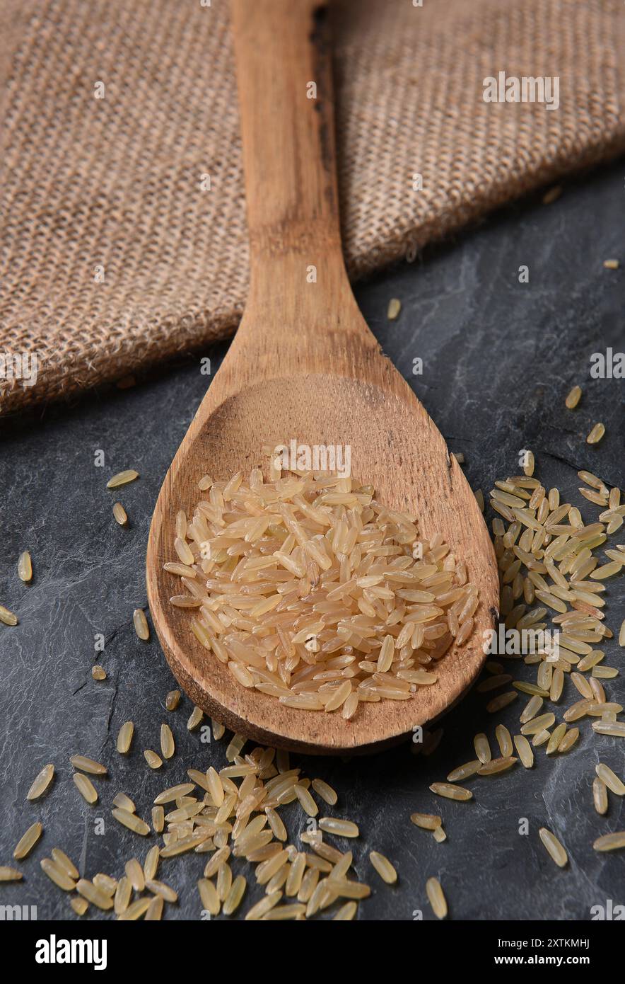 Nahaufnahme eines Holzlöffels mit braunem Reis, auf Schiefergrund und Sacksack. Stockfoto