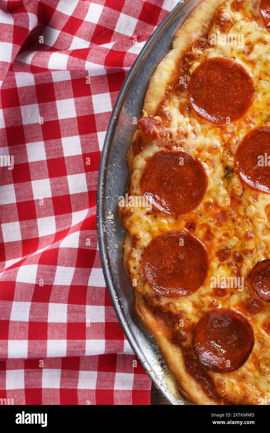 Frische hausgemachte Pizza auf rot-weiß kariertem Tischtuch auf einem Holztisch mit Kopierraum, vertikales Format. Stockfoto