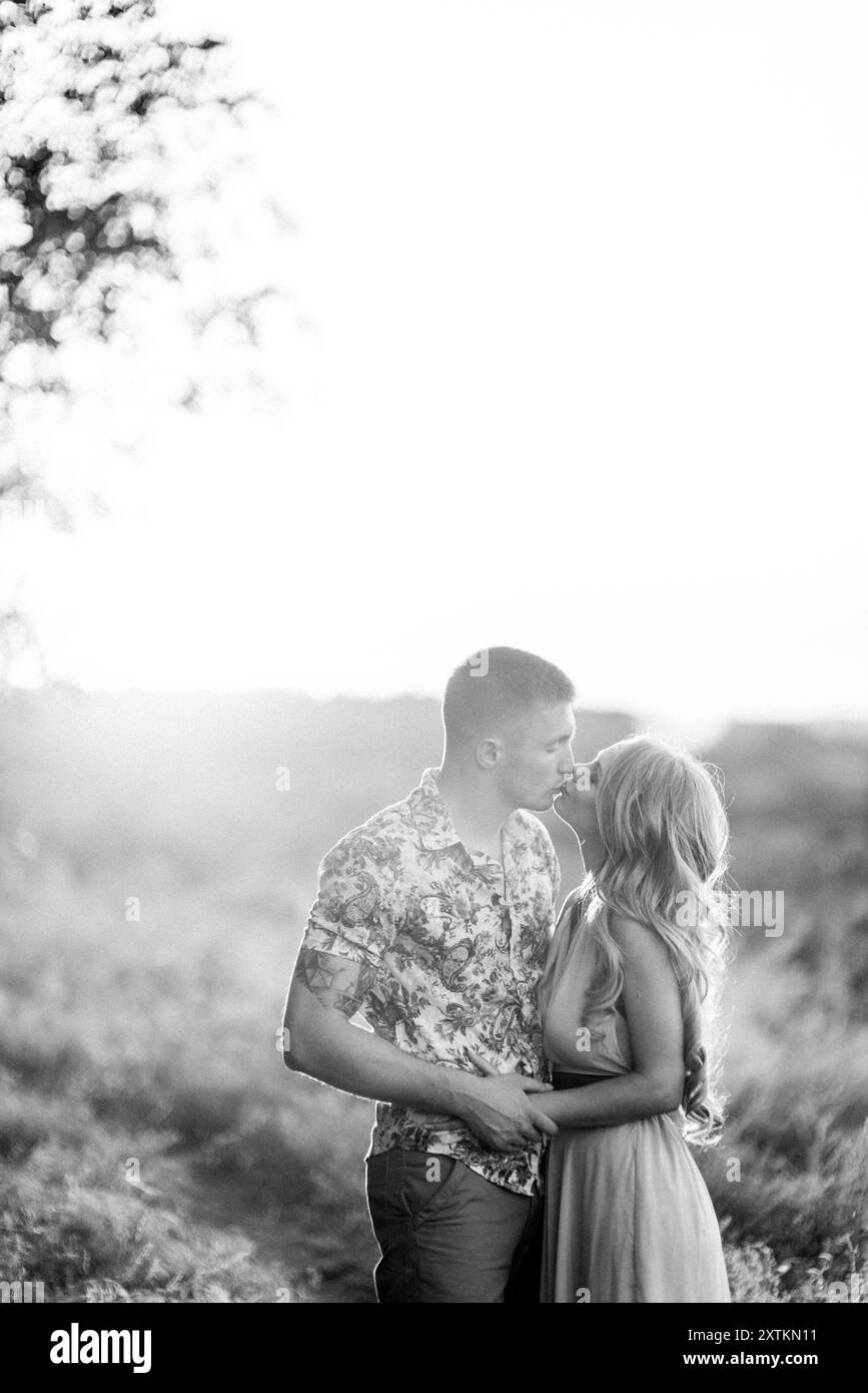 Blonde Mädchen mit losen Haaren in einem hellblauen Kleid Und ein Kerl im Licht des Sonnenuntergangs in der Natur Stockfoto