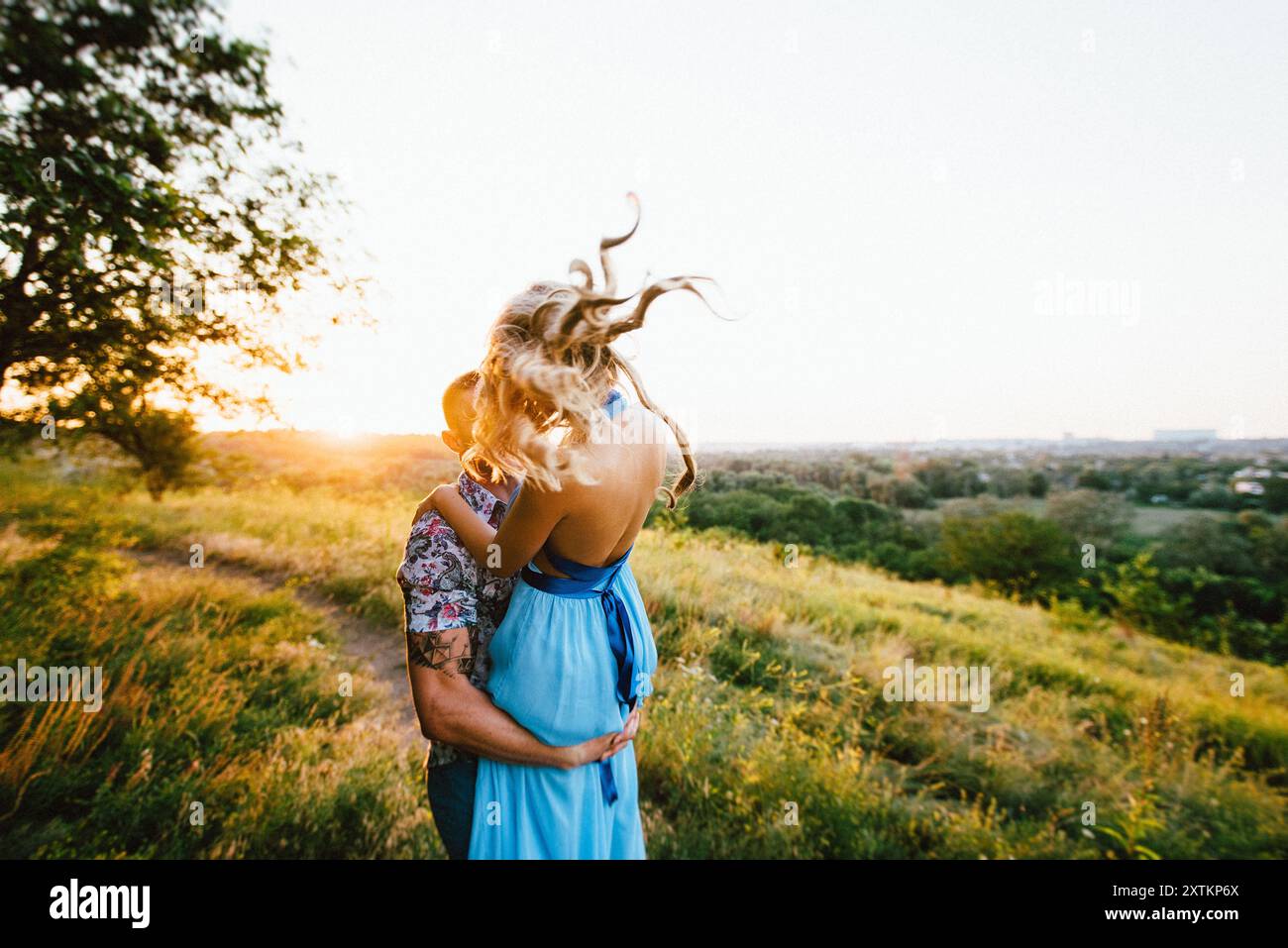 Blonde Mädchen mit losen Haaren in einem hellblauen Kleid Und ein Kerl im Licht des Sonnenuntergangs in der Natur Stockfoto