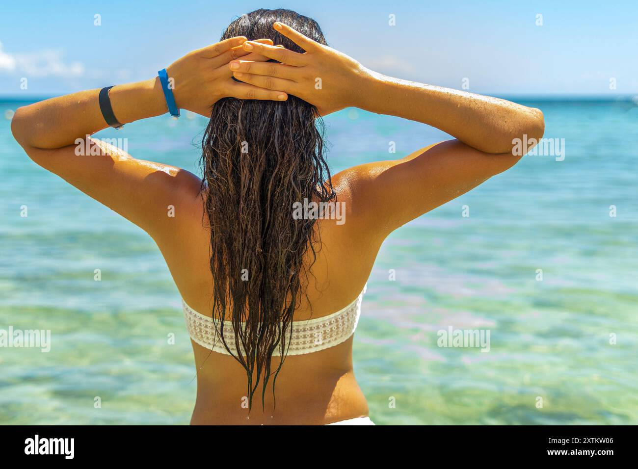 Sommerschönheit, während sie sich in der Sonne und im Wind der Karibik sonnt. Ihre atemberaubende Figur und das fließende Haar werden perfekt durch die atemberaubende Landschaft ergänzt Stockfoto