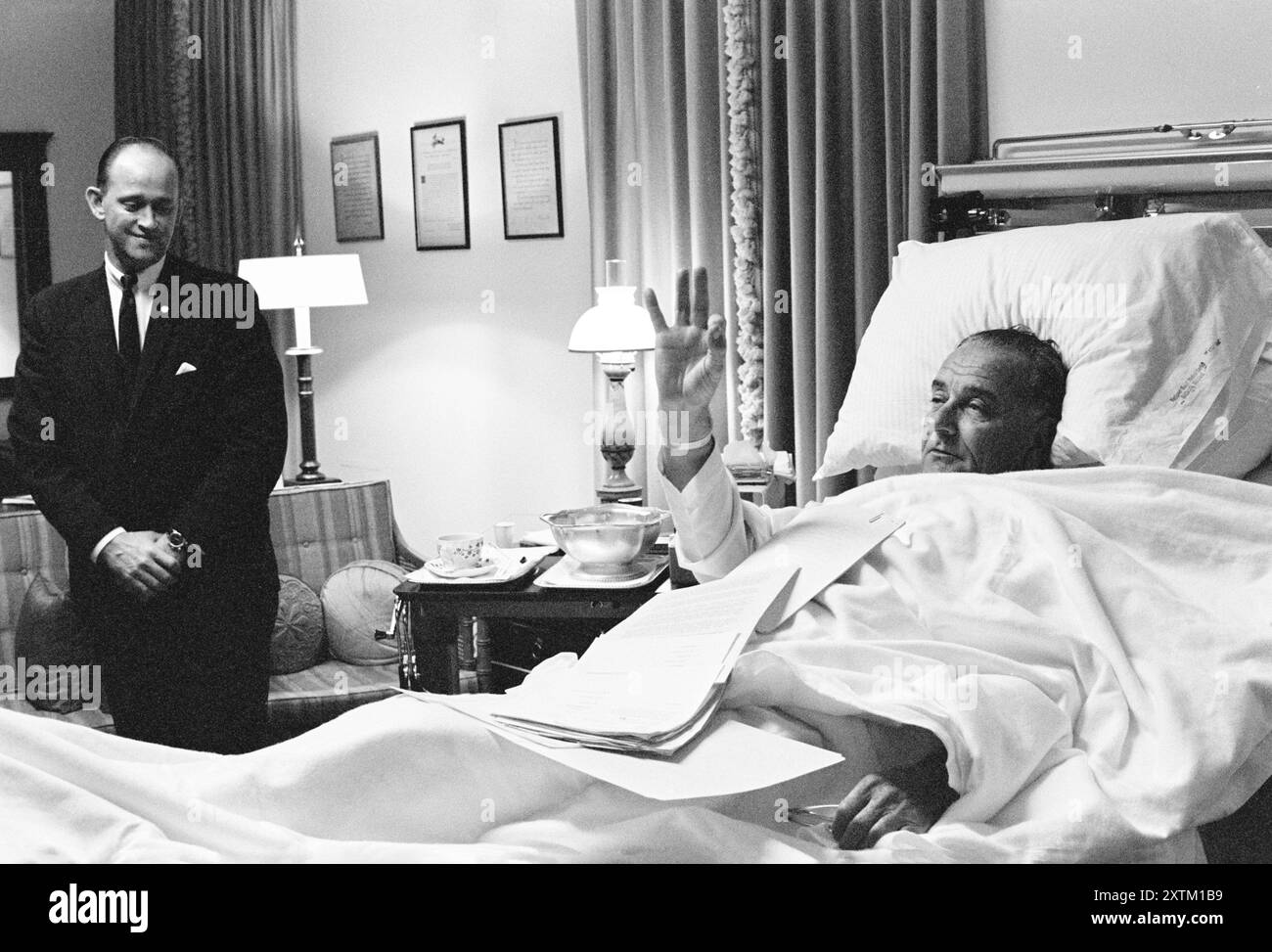 Paul Glynn sieht als US-Präsident Lyndon Johnson, der nach einer Operation zur Entfernung von Kehlkopfpolypen ein OK-Zeichen von seinem Krankenhausbett gibt, National Naval Medical Center, Bethesda, Maryland, USA, Robert Knudsen, November 1966 Stockfoto