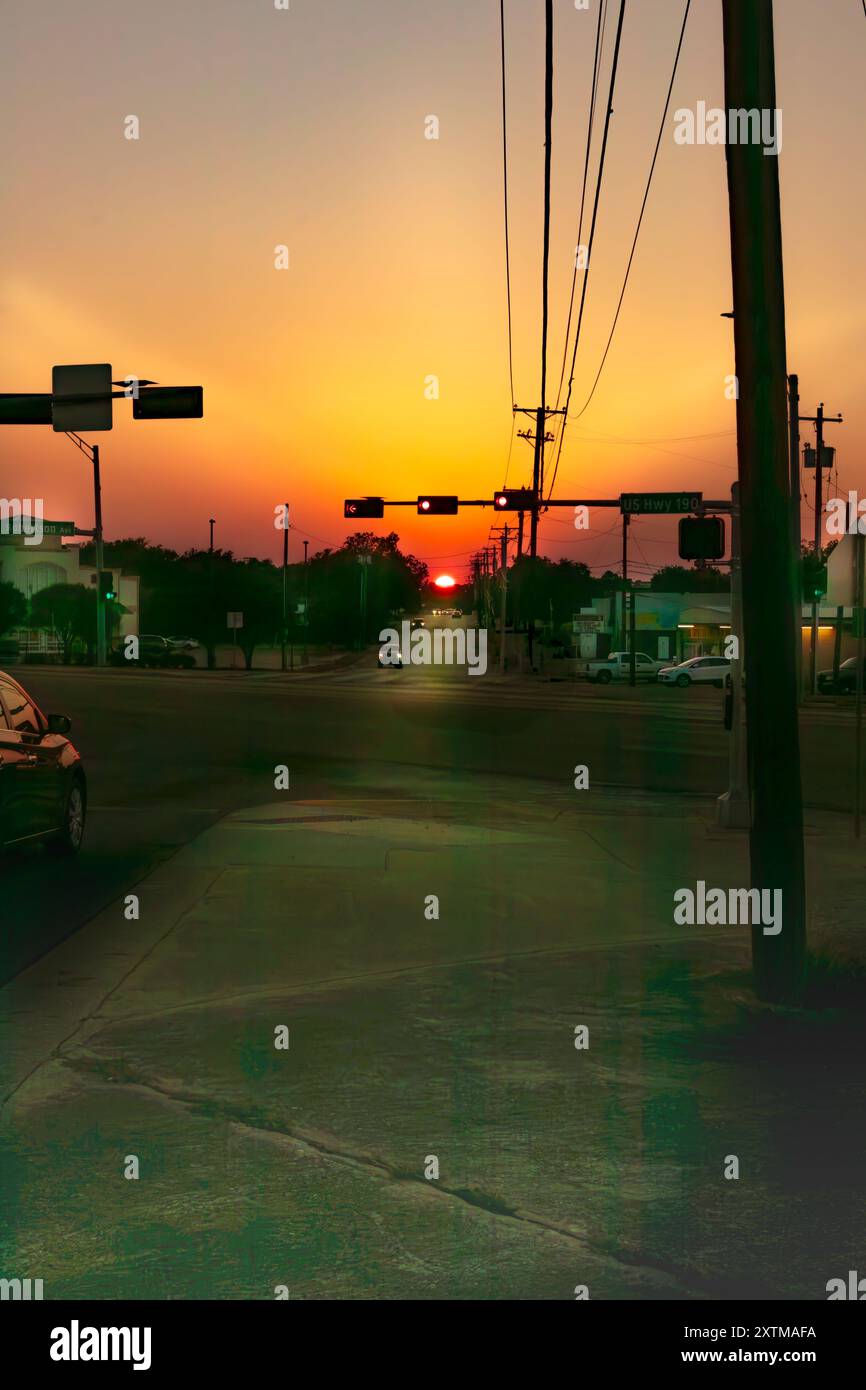 Die Sonne steht tief am Horizont und strahlt ein warmes, goldenes Licht auf der anderen Straßenseite aus, gesäumt von Gebäuden und Autos. Stockfoto