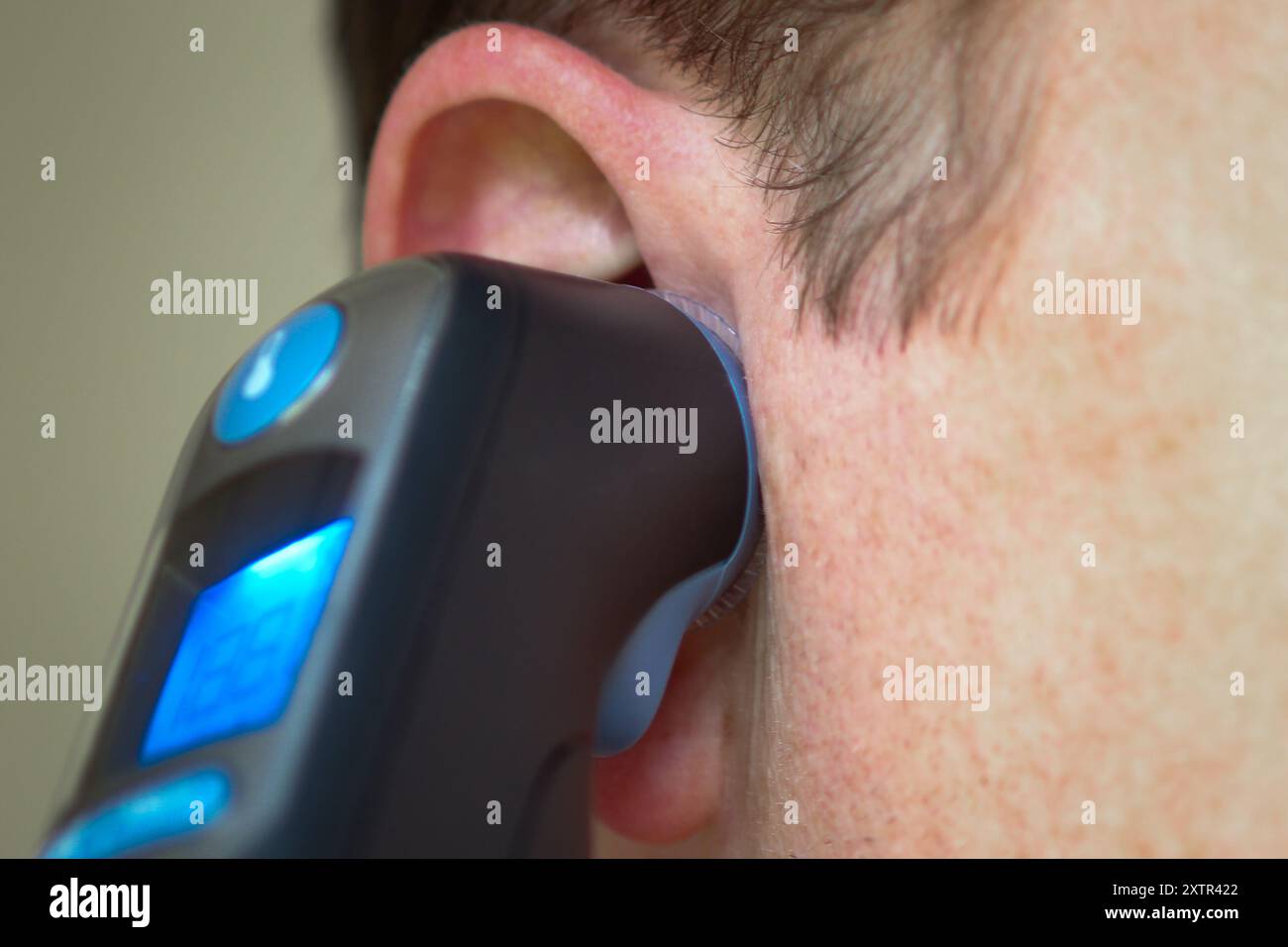 Nahaufnahme eines Mannes, der seine Temperatur mit einem digitalen Ohrthermometer überprüft Stockfoto