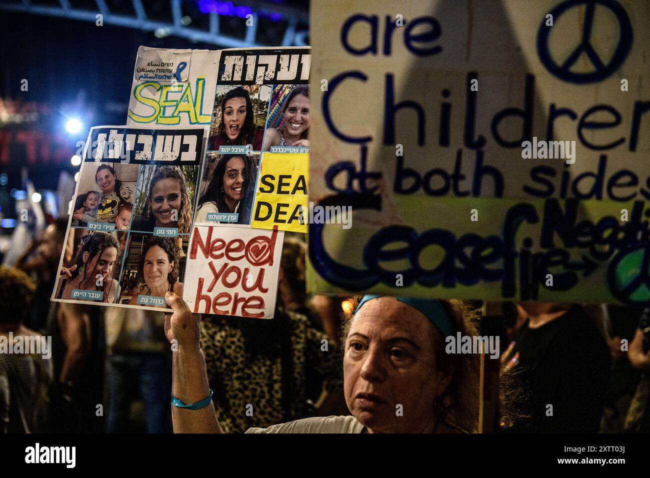 Israel. August 2024. Eine Aktivistin, die „Frauen für den Frieden“ hält Schilder mit den Fotos der israelischen Geiselinnen hoch, auf denen steht „Need you here“ und „Seal the Deal“, und ein weiteres Schild mit der Aufschrift: „Sie sind Kinder auf beiden Seiten. Waffenstillstandsverhandlungen“. Die Israelis demonstrierten mit den Familien der Geiseln gegen Premierminister Benjamin Netanjahu und forderten ein sofortiges Geiselabkommen und einen Waffenstillstand - während in Katar Verhandlungen über den Waffenstillstand im Gazastreifen stattfinden. Tel Aviv, Israel. August 2024. (Matan Golan/SIPA USA). Quelle: SIPA USA/Alamy Live News Stockfoto