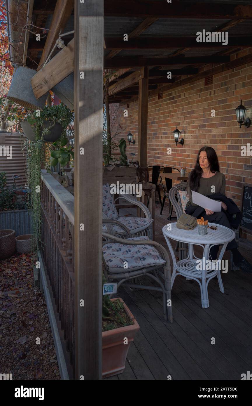 Eine Reisende sitzt auf der Veranda eines hübschen Country Town Store & Coffee Shop, während sie nachdenklich über das friedliche Ambiente ihres Standorts nachdenkt. Stockfoto