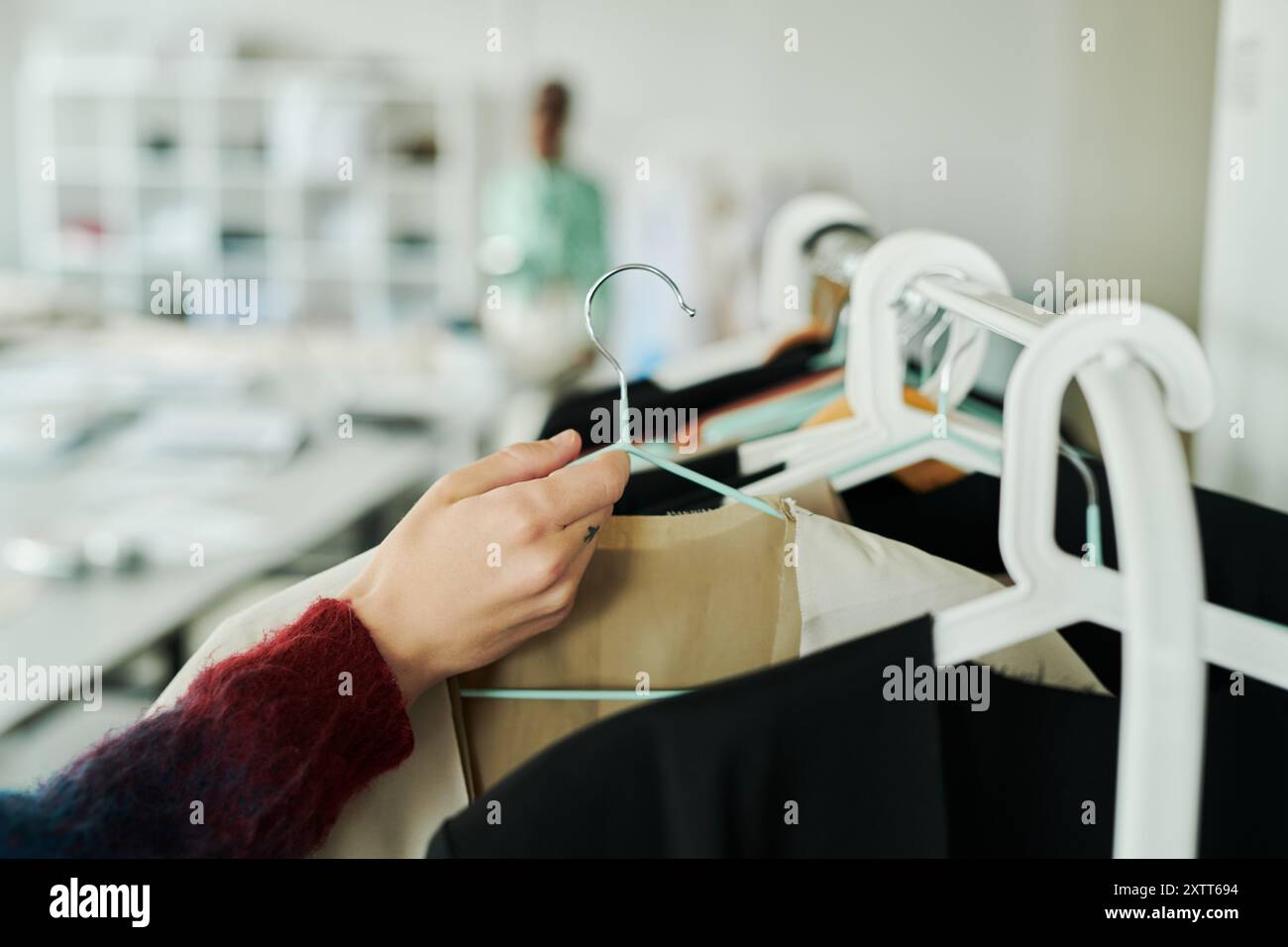 Hand eines jungen männlichen Modedesigners oder Stylisten, der Kleiderbügel mit unvollendetem Blazer aus der neuen Saison-Kollektion von Rack trägt Stockfoto