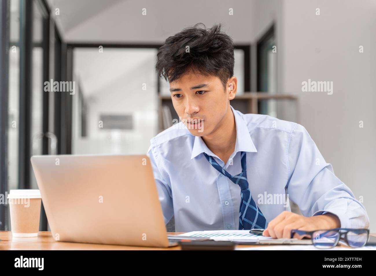 Müder junger Geschäftsmann, der spät im Büro arbeitet und versucht, die Frist für sein Projekt einzuhalten Stockfoto